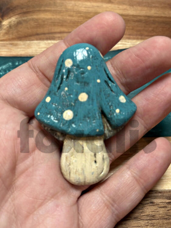 A photo of a sculpted and painted mushroom. It is painted with a blue cap with cream spots and a cream-colored stem.