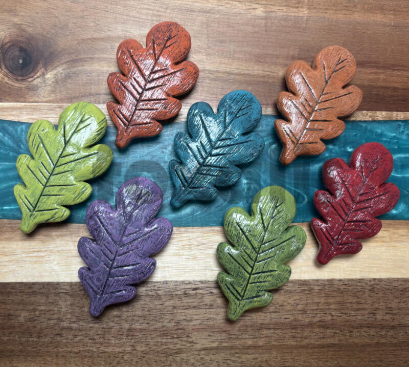 A set of seven sculpted and cast leaves painted in a variety of colors.